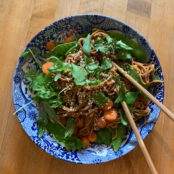 Asian noodles served in a blue and white bowl and topped with snow peas, carrots, and sesame seeds 