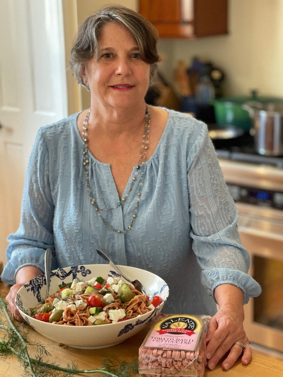 Mary Ann serving a tomato basil fettuccine Greek salad recipe in a blue and white bowl
