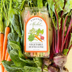 Vegetable Fettuccine in a clear bag surrounded by fresh vegetables as well on the label with a orange border.