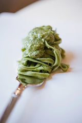 Spinach linguine twirled around a fork with pesto on top